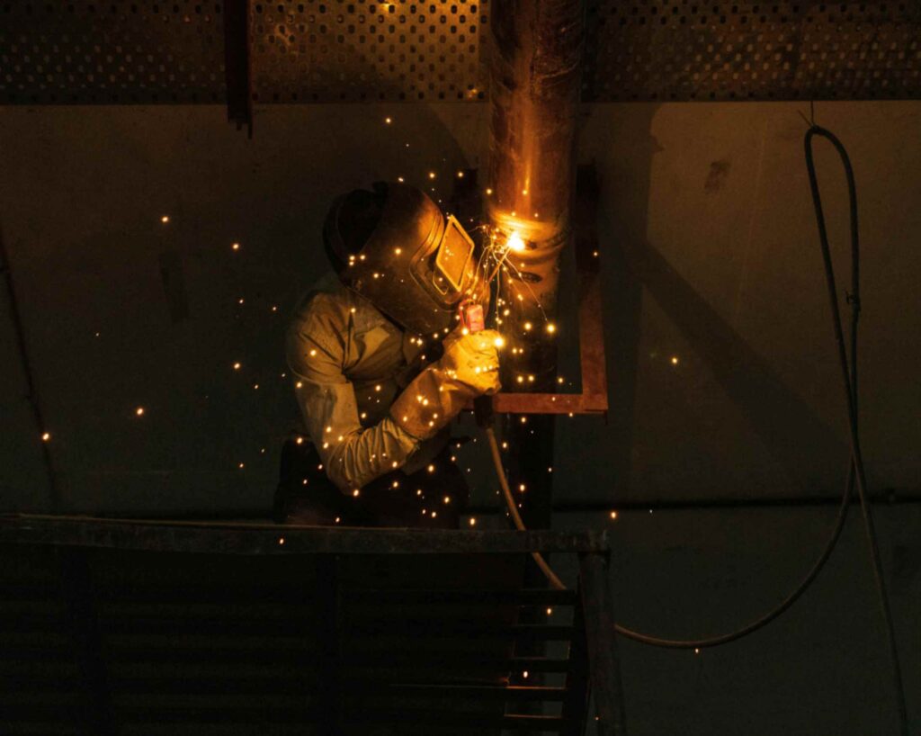 Welder performing pipe welding with sparks in a workshop setting